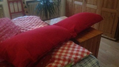 Ein rotes Umarmkissen liegt auf dem Bett aus karierten Decken, umgeben von einer warmen, heimeligen Schlafzimmeratmosphäre.