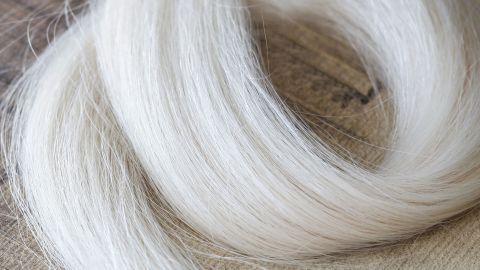 Helle Haare liegen sanft auf einer Holzoberfläche und zeigen die Wirkung einer schonenden Farbveränderung ohne Blondierung.