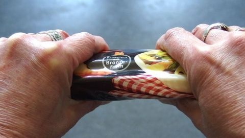 Zwei Hände brechen Spaghetti, während sie die Verpackung zusammendrücken, in einer neutralen Umgebung.