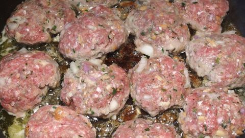 Bouletten braten in einer Pfanne, umgeben von frischem Gemüse, bieten eine herzhafte Mahlzeit in geschmackvollem Umfeld.