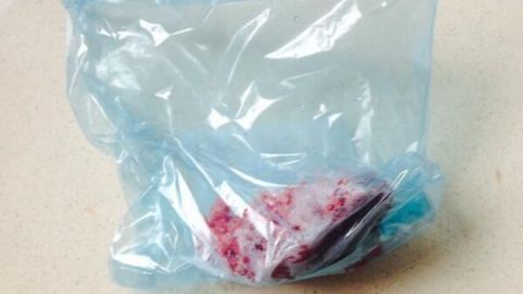 Eine Plastikfolie enthält rotes, tiefgefrorenes Hundefutter und liegt auf einer hellen Küchenarbeitsplatte.