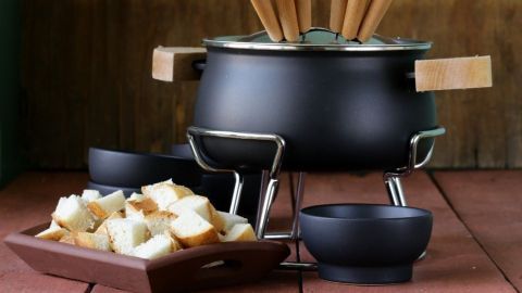 Ein Käsefondue-Topf steht auf einem rustikalen Tisch, umgeben von frisch geschnittenem Brot, bereit zum Genießen.