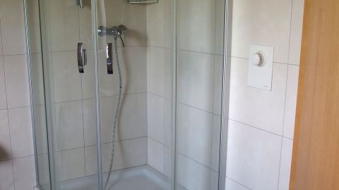 Kalkbildung in Duschkabinen nach jedem Duschen mit heißem Wasser verringern. Eine durchsichtige Duschkabine steht in einem Badezimmer, mit Fliesenwänden und einem Duschkopf, bereit zur Nutzung.