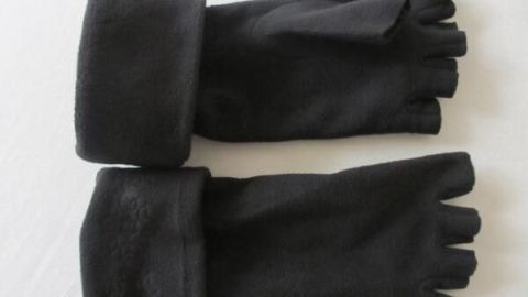 Schwarze Fleecehandschuhe liegen flach auf weißem Hintergrund, zeigen abgeschnittene Finger und umgeschlagene Bündchen.