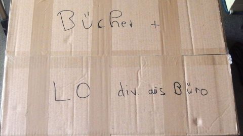 Ein Umzugskarton mit der Aufschrift "Bücher" und "Lö div. aus Büro" steht bereit, um das Packen zu erleichtern.