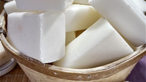Weißes Seifenstück liegt in einem geflochtenen Korb, umgeben von weiteren Seifenstücken in einem Marktumfeld.