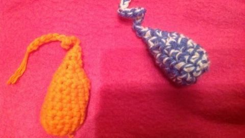 Gehäkeltes Katzenspielzeug in Form von zwei bunten Fischen liegt still auf einem pinken Stoff.