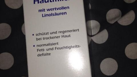 Eine Packung "Linola Hautmilch" liegt auf gepunktetem Stoff. Sie verspricht Schutz und Regeneration bei trockener Haut.