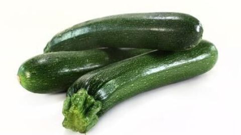Drei frische Zucchini liegen auf einer weißen Oberfläche, bereit zur Verarbeitung in einem süßen Zucchinikuchen.