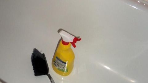 Ein gelber Sprühflakon und Handfeger liegen in einer weißen Badewanne mit rosa Fliesen im Hintergrund.
