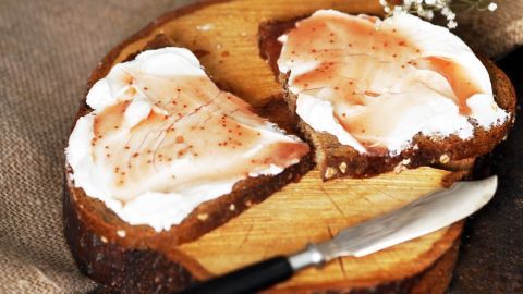 Zwei Brotscheiben sind mit frischem Frischkäse und einer dünnen Schicht Schinken belegt. Ein Messer liegt daneben.