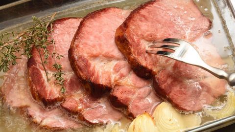 Eine große Fleischpfanne mit saftigem Fleisch und Zwiebeln wird serviert, umgeben von Kräutern und Brühe.