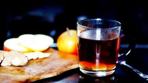 Ein Glas heißer Apfelsaft mit Ingwer steht auf einem Holzbrett, umgeben von geschnittenen Äpfeln und einer ganzen Apfel.