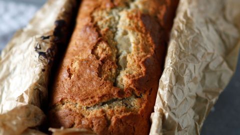 Das frisch gebackene Dinkel-Bananenbrot liegt in Papier eingewickelt auf einer grauen Oberfläche und wirkt appetitlich.