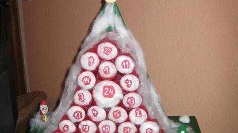 Ein selbstgemachter Adventskalender aus roten, nummerierten Rollen, in Pyramidenform arrangiert, steht auf einem Tisch.