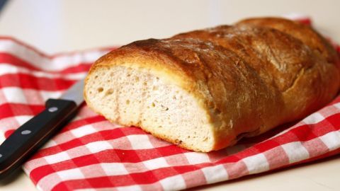 Ein frisch gebackenes Weißbrot liegt auf einem rot-weiß karierten Tuch, während ein Messer daneben bereitliegt.