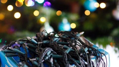 Eine Lichterkette liegt unordentlich auf einem weißen Teppich, umgeben von einem Weihnachtsbaum mit bunten Lichtern.