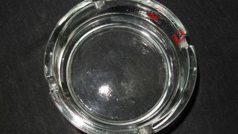 Ein dreckiger Aschenbecher liegt auf einem schwarzen Untergrund, bereit zum Reinigen und Entfernen von Abfällen.