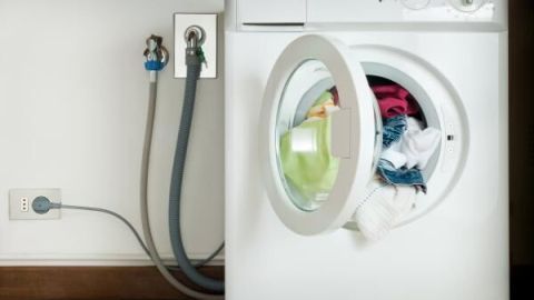 Eine Waschmaschine mit geöffnetem Bullauge, die bunte Wäsche wäscht, steht in einem modernen Waschraum.