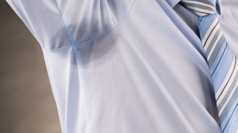Ein Mann in einem hellblauen Hemd mit sichtbaren Schweißflecken unter den Achseln steht ernst und zeigt seine Probleme mit Schwitzen.