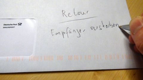 Eine Hand hält einen Stift und schreibt auf einen Briefumschlag, der für ein Werbeschreiben verwendet wird.