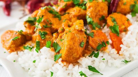 Ein Teller mit thailändischem Curry und Reis, garniert mit frischen Kräutern, serviert auf einem weißen Geschirr.