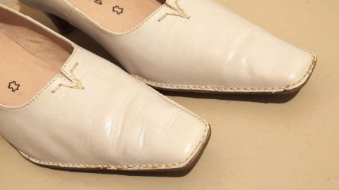 Weiße Schuhe liegen auf einem hellen Untergrund und zeigen dunkle Streifen, die entfernt werden sollen.