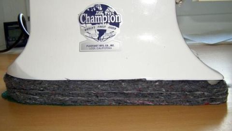 Entsafter ruht auf dicker Filzunterlage zur Geräuschdämmung auf Holztisch; Etikett: "The Champion, World's Finest Juicer."