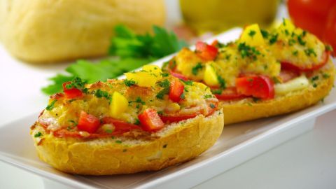 Knusprige Brötchen mit buntem Gemüse, garniert mit Kräutern, liegen auf einem weißen Teller vor einem hellen Hintergrund.