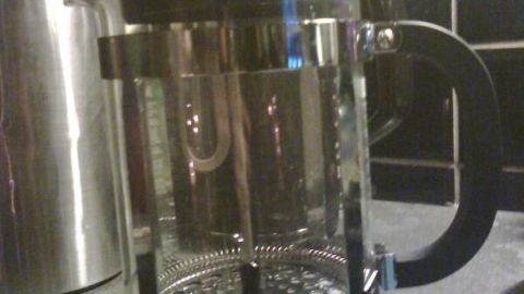 Eine leere French Press steht auf einer Küchenarbeitsplatte mit Fliesen im Hintergrund.