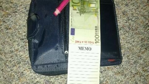 Ein schwarzes Portemonnaie liegt auf einem Teppich. Darauf ein rosa Kugelschreiber, ein 100-Euro-Schein und ein leerer Memo-Einkaufszettel.