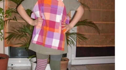 Ein Kind in einem Pippi Langstrumpf-Kostüm trägt bunte Kleidung und Zöpfe, steht in einem Wohnzimmer mit Pflanzen.