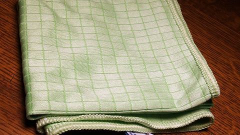 Ein grünes Geschirrhandtuch aus Mikrofaser liegt ordentlich gefaltet auf einer Holzoberfläche, bereit zum Einsatz in der Küche.