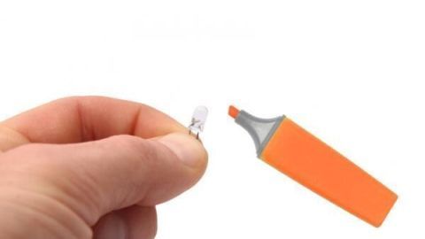 Eine Hand hält eine kleine LED-Lampe, während ein orangefarbener Marker daneben gezeigt wird, um sie zu markieren.