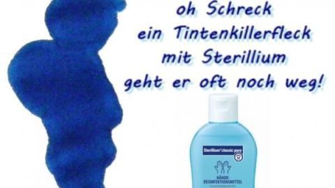 Ein blauer Tintenkiller-Scherzfleck neben einer Flasche Sterilium, mit Text über das Entfernen von Tintenkiller-Flecken.