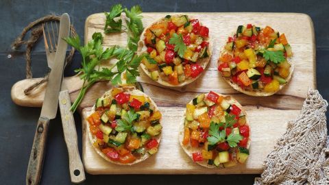 Drei knusprige Kartoffelpuffer sind mit buntem, frischem Gemüse belegt und auf einem Holzbrett angerichtet.