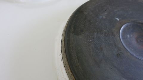 Ist einmal Plastikfolie auf den Herd gelangt, kann man diese mit Nagellackentferner gut beseitigen. Eine Metallplatte des Herdes hat Klebereste, die mit Nagellackentferner entfernt werden sollen, auf einem weißen Untergrund.