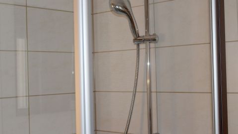 Eine Dusche mit glänzender Armatur steht in einem hellen Badezimmer; der Essigreiniger wird zur Reinigung sprüht.