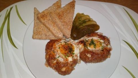 Auf einem weißen Teller liegen zwei knusprige Eiergerichte mit einem Eigelb, dazu Toast und Gurken.