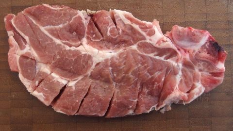 Eine Scheibe Fleisch liegt auf einem Holzbrett, mit ziselierten Schnitten, bereit zum Kochen in einer Küche.