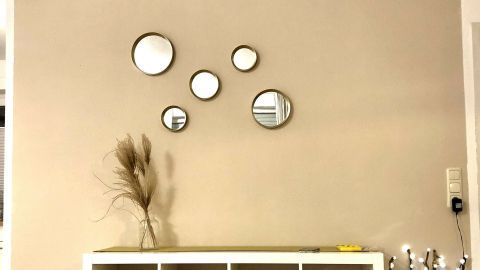 Eine decorierte Wand zeigt mehrere Spiegel, die an einem hellbeigen Hintergrund hängen, um einen modernen Raum zu verschönern.