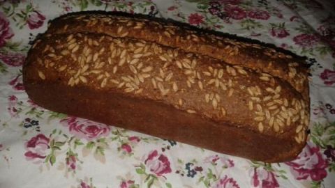 Ein Dinkel-Buttermilchbrot liegt auf einem blühenden Tuch und präsentiert seine goldene, knusprige Kruste mit Saaten.