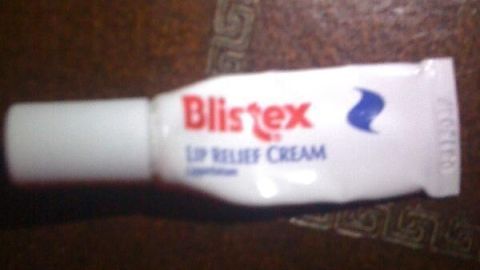 Eine kleine Tube Blistex Lip Relief Cream liegt auf einem dunklen Holztisch.