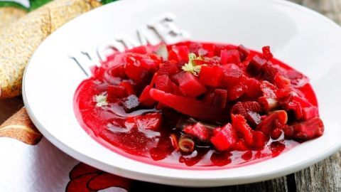 Eine bunte Rote-Bete-Suppe liegt in einer weißen Schale auf einem rustikalen Holztisch, garniert mit Kräutern.