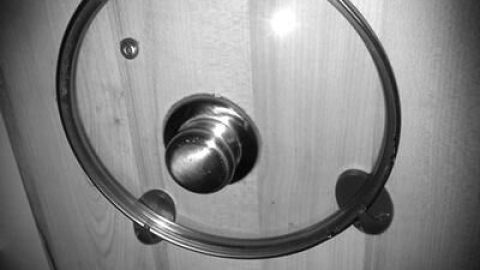 Ein Topfdeckel hängt fixiert an einem Holztürknauf, um Platz zu sparen.