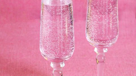 Zwei Sektgläser mit Bläschen stehen auf einer pinken Tischdecke und wirken frisch und sprudelnd.