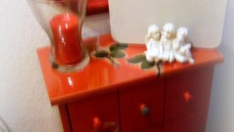 Ein roter Schrank steht im Flur, darauf liegen eine digitale Waage und Dekoration. Der Raum reflektiert einen persönlichen Stil.