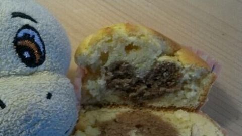 Ein Muffin mit sichtbarem Herzmuster wird aufgeschnitten. Daneben ist ein Stofftier, auf einem Holztisch liegend.