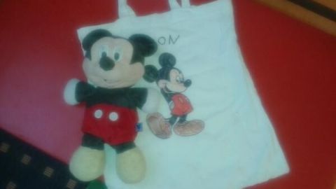 Eine bemalte Stofftasche liegt auf einem roten Tisch, daneben ein Mickey-Mouse-Stofftier, das fröhlich schaut.