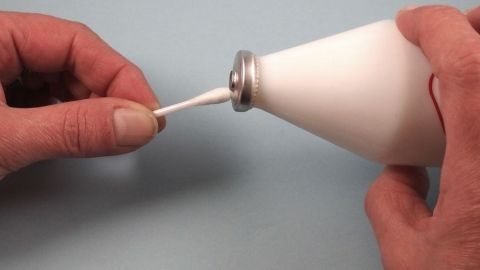Eine Hand hält ein Wattestäbchen, das gerade in eine Tube mit Creme eingeführt wird, um Lippenherpes schnell zu behandeln.